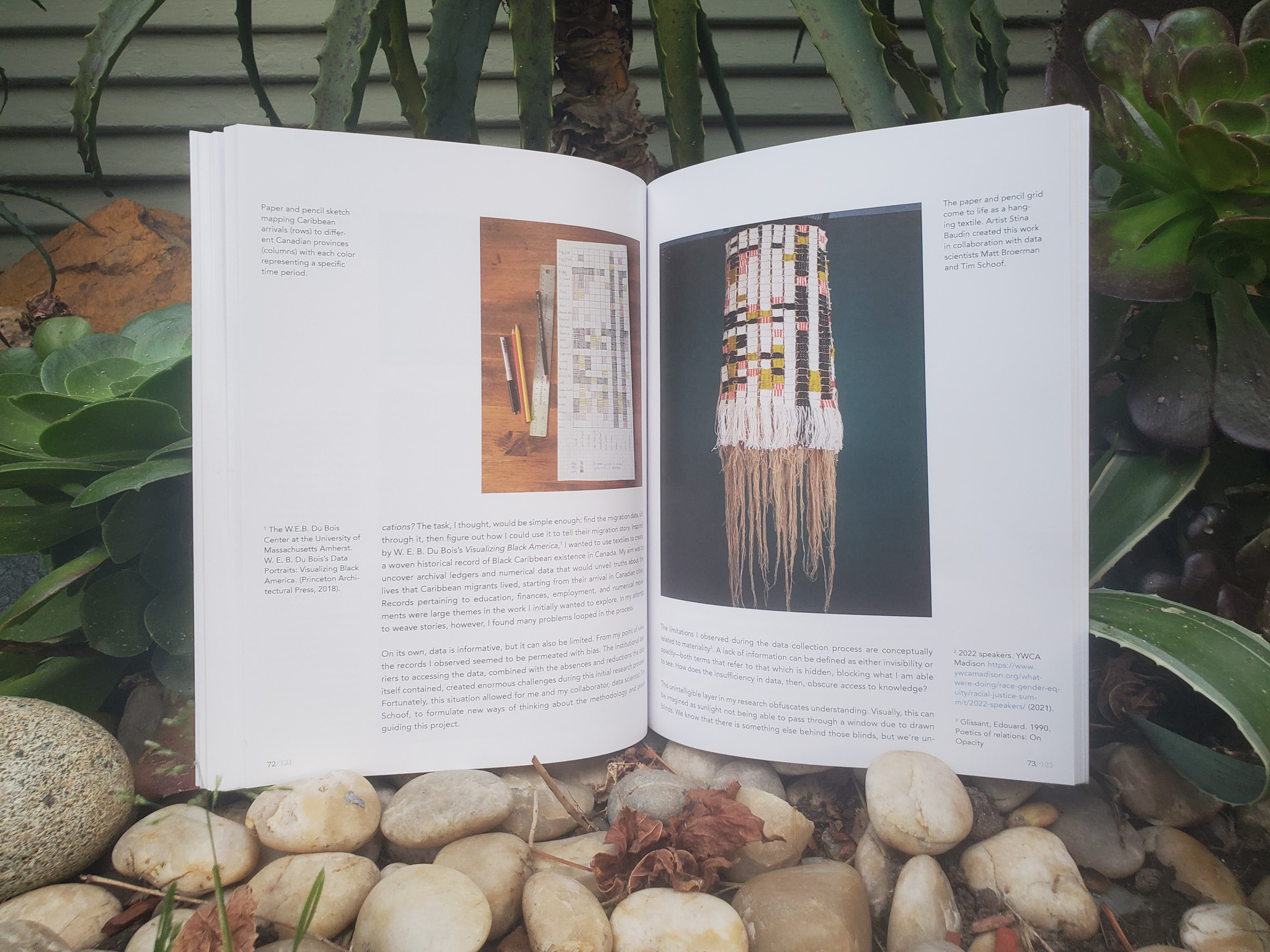 Photograph of an open book with two full page art works in a garden