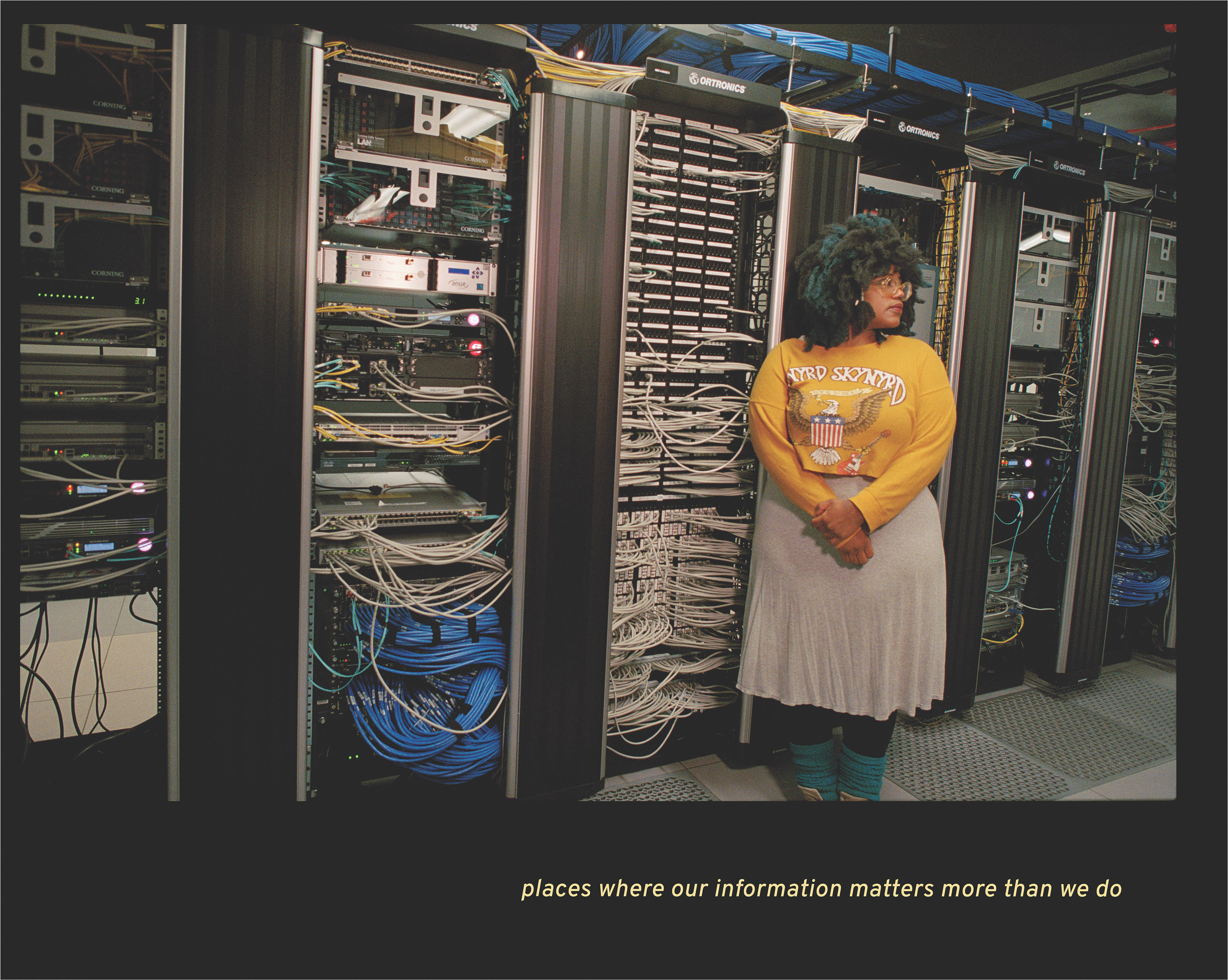Black woman with black and blue hair stands in front of a large row servers with the caption “places where our information matters more than we do”